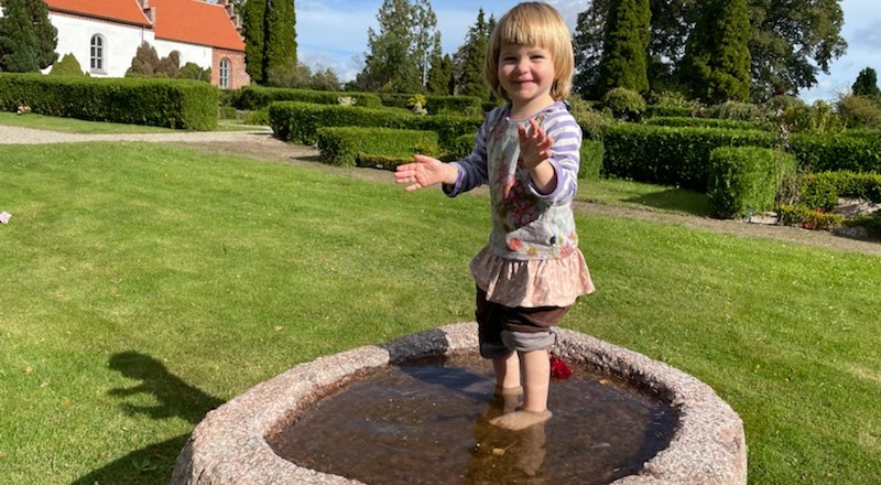 Dåbslund på Jørlunde Kirkegård Barn stående i døbefont udenfor
